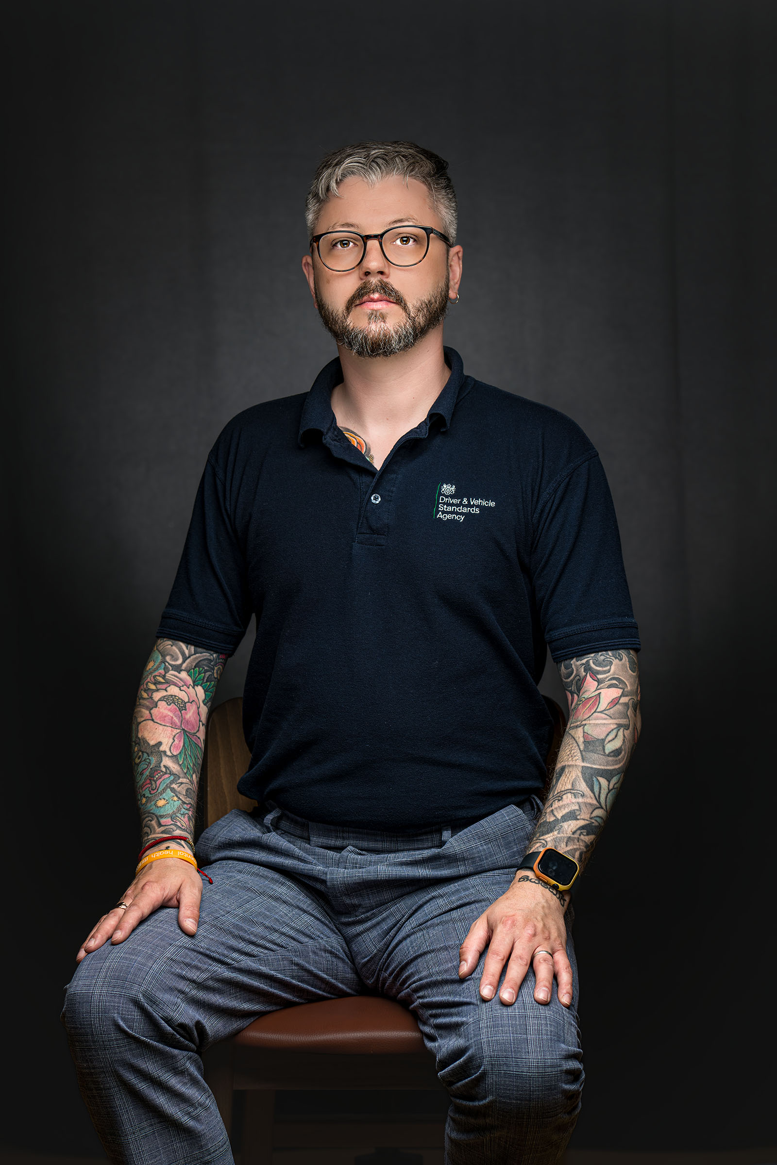 Seated professional portrait of a man with glasses and tattooed arms