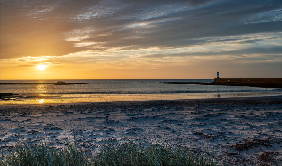 Lighthouse on a harbour wall beneath a warm sunset