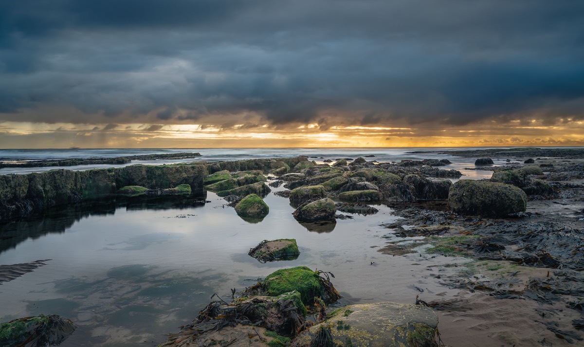 Rock pools and seaweed beneath a stormy coastal sky