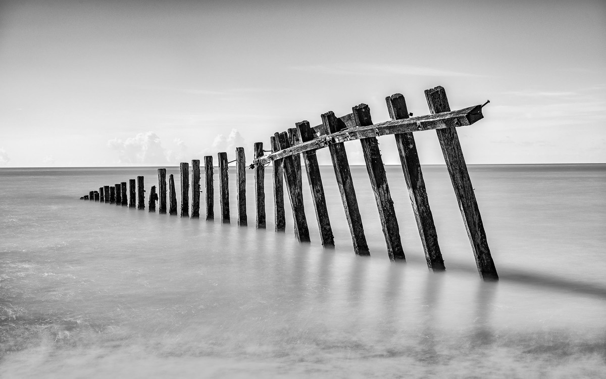 Curving timber sea defence disappearing into still coastal water
