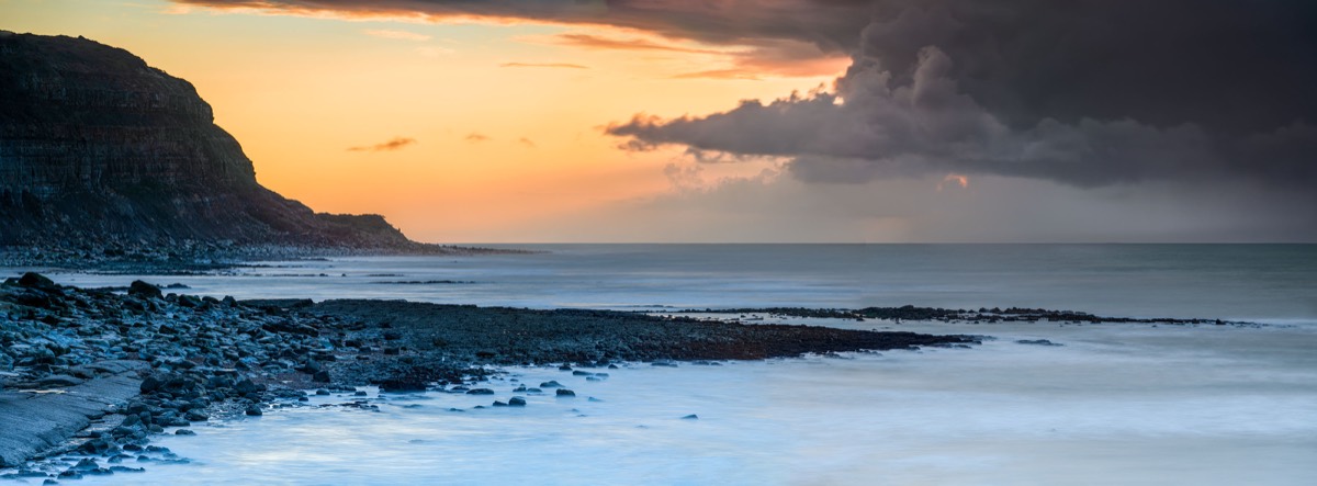 Wide stormy coastal panorama beneath layered cloud