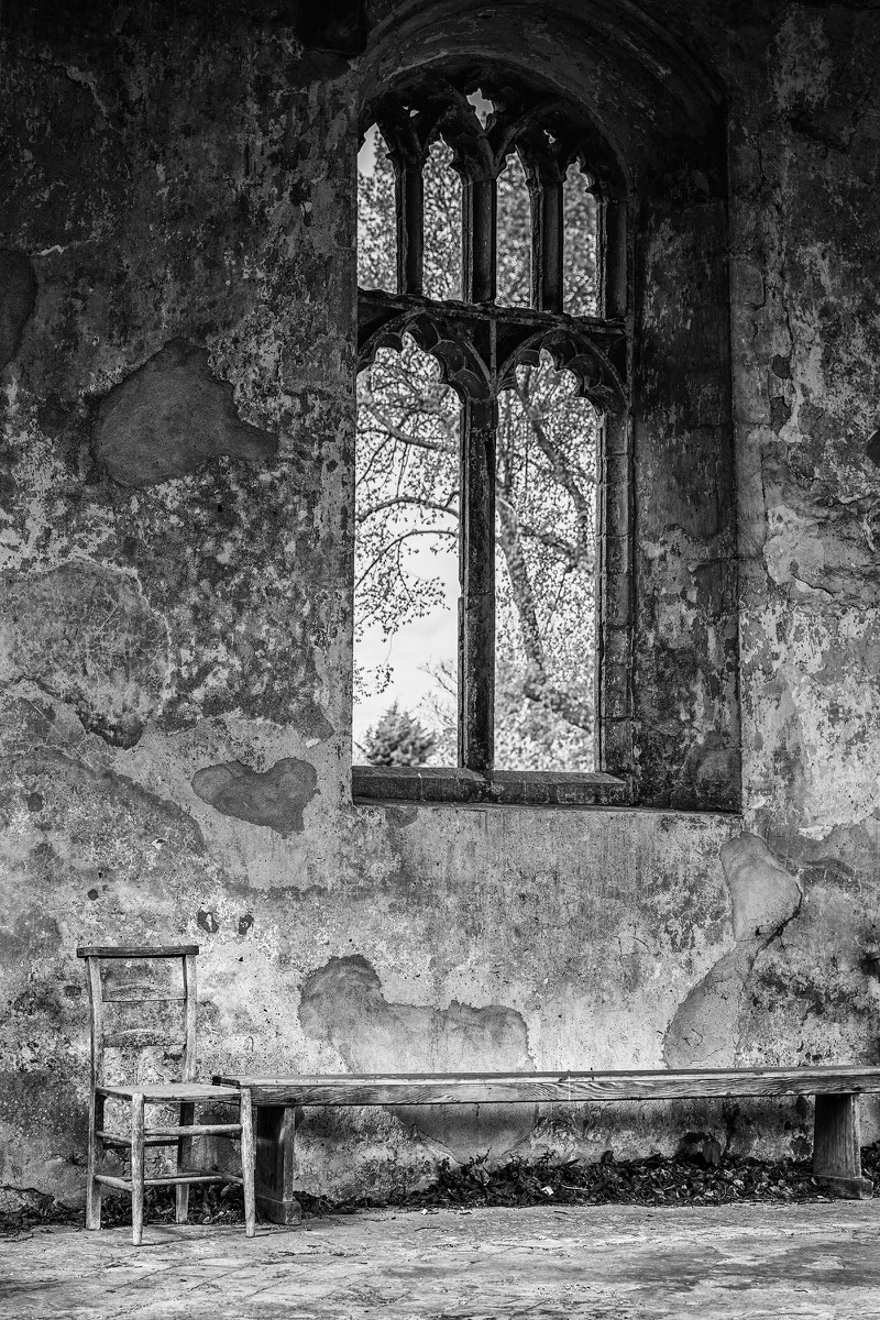 Tall church window above a chair and wooden bench